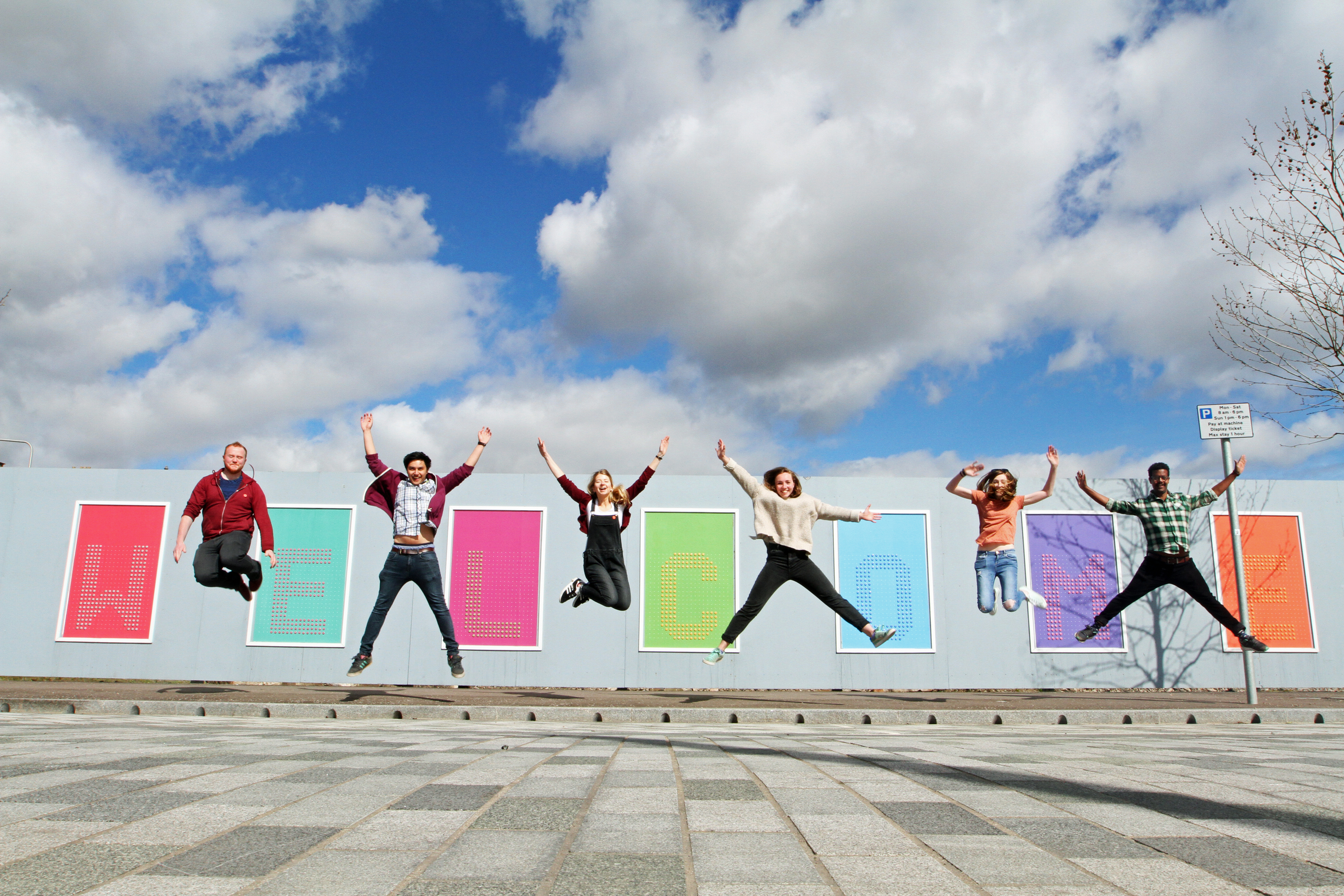 Volunteers  Aaron Donald, Ibrahim Karim, Sarah Duffy, Zoe Broughton, Ali Elliott and Aki Nikulainen celebrate as removable pin badges are installed in Slessor Gardens  to read 'All Welcome Here' .