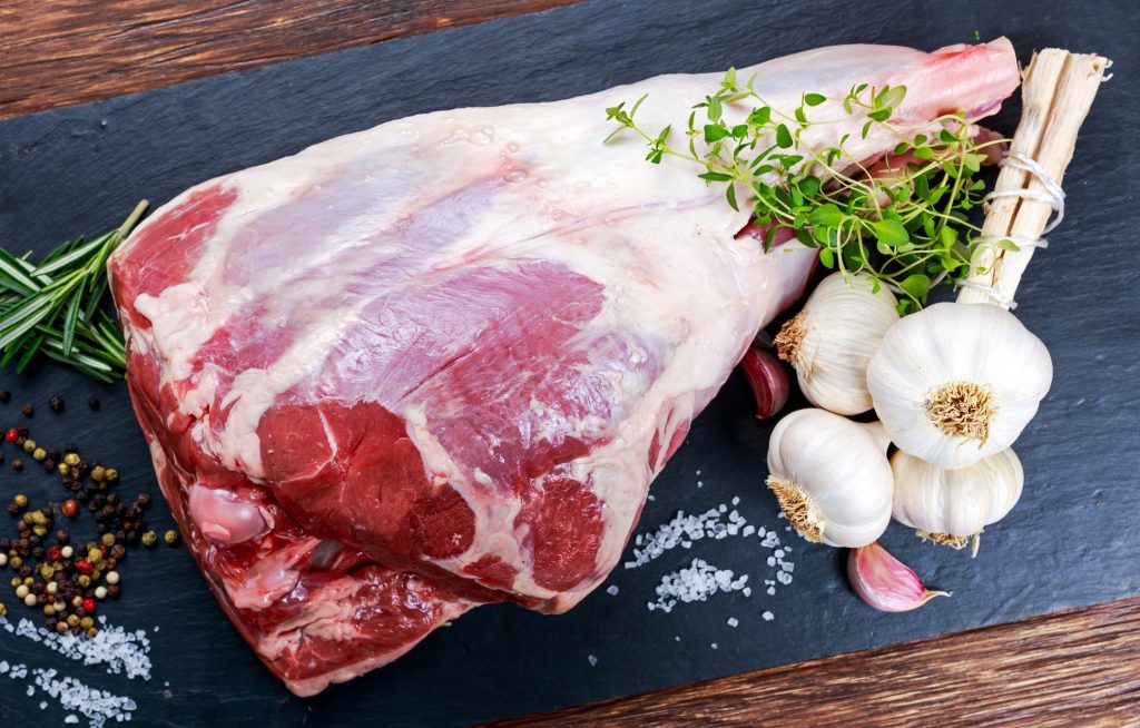Raw lamb leg on blue stone background with herbs