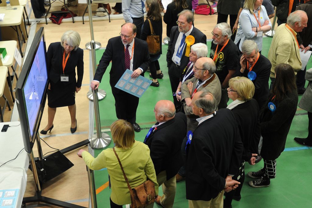Returning officer Richard Stiff (centre back left) candidates and agents watching the adjudication screen.
