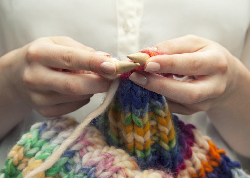 Young woman knitting a woolen colorful scarf, closeup