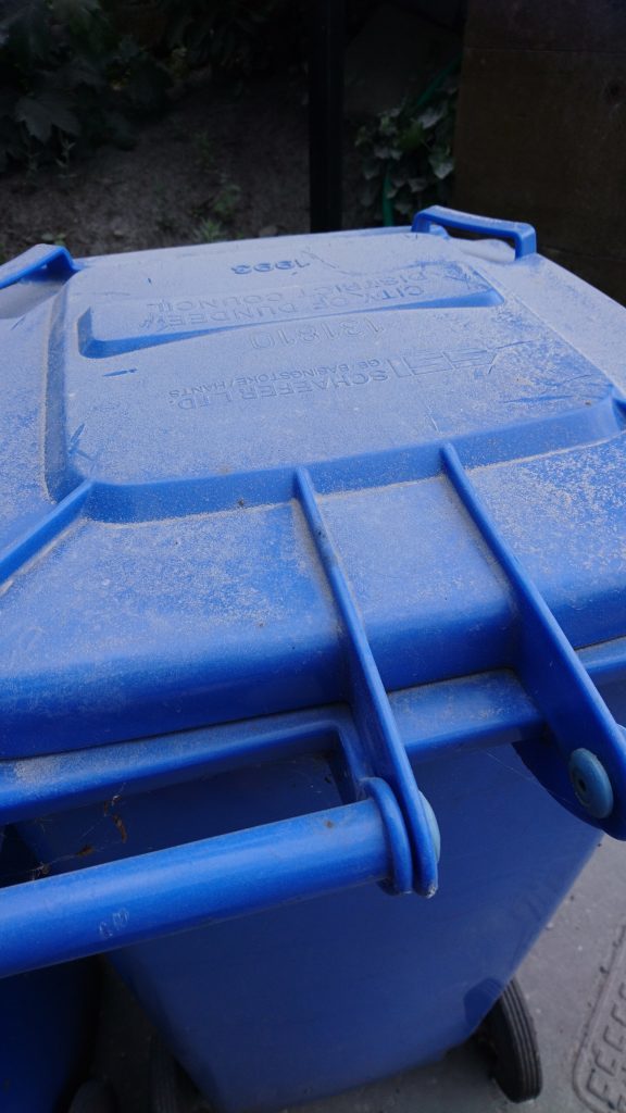A blue wheelie bin covered in dust at the side of Perth Road.