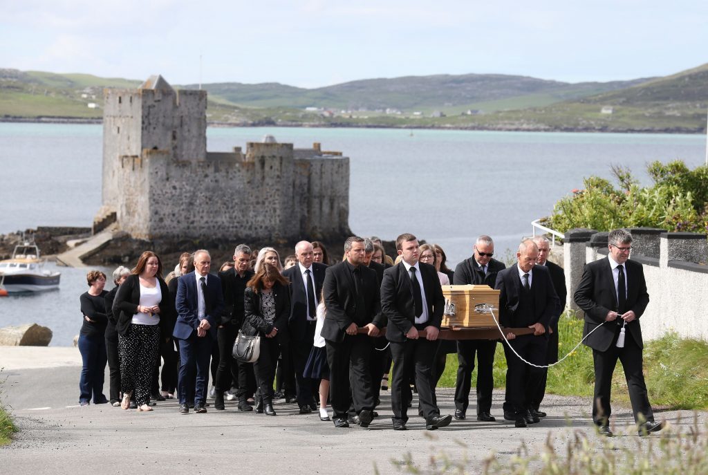 Funeral procession passes Kisimul Castle on its way to the Church of Our Lady, Star of the Sea, in Castlebay.