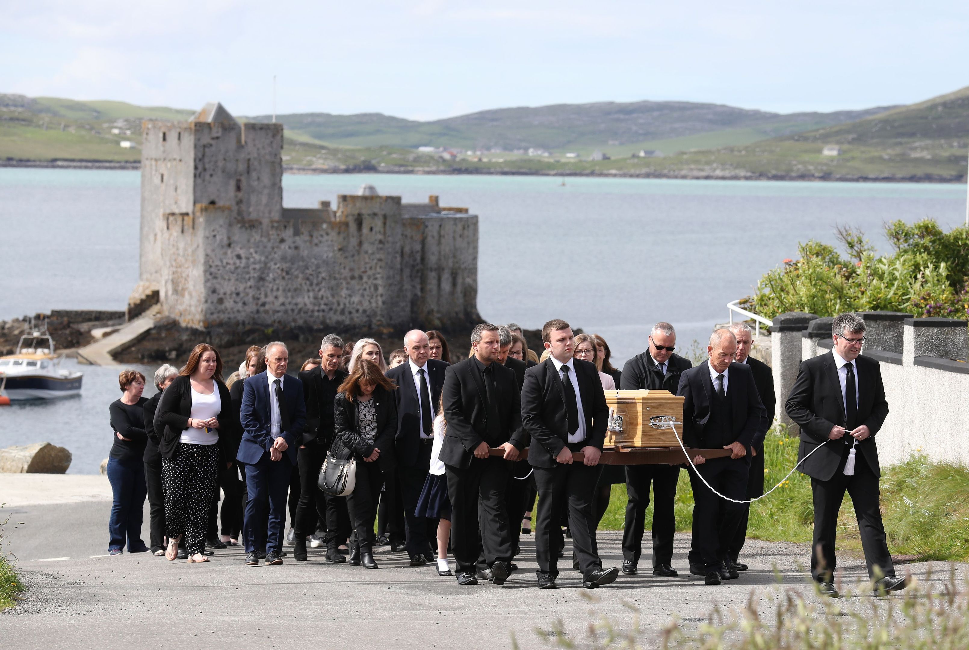 Funeral procession passes Kisimul Castle on its way to the Church of Our Lady, Star of the Sea, in Castlebay.