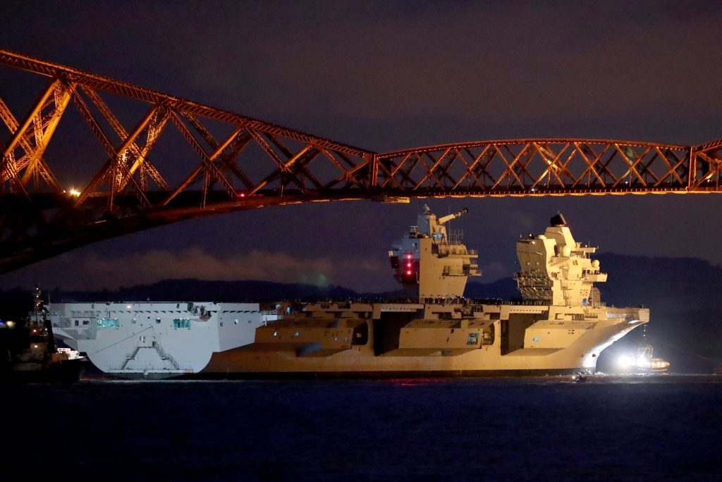 The ship is pulled by tugs under the Forth Rail Bridge in the Firth of Forth, as she sets sail to begin her sea trials. 