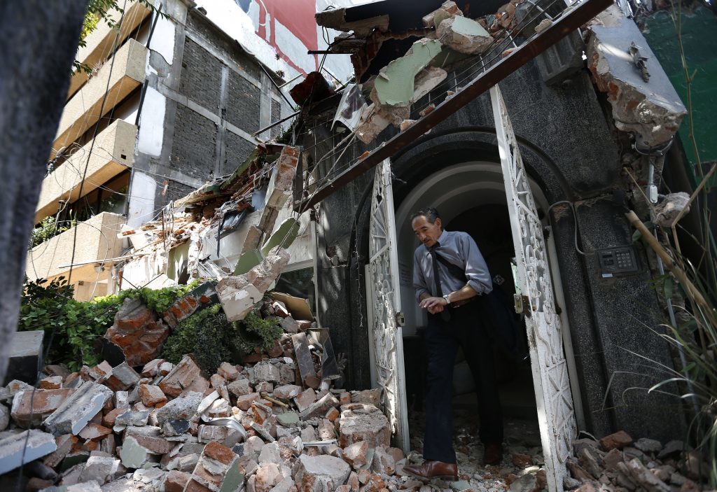 A man walks out of the door frame of a building that collapsed after an earthquake