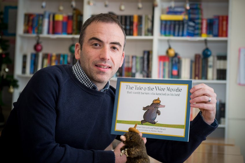 Matthew Mackie holding his previous book, The Tale o the Wee Mowdie