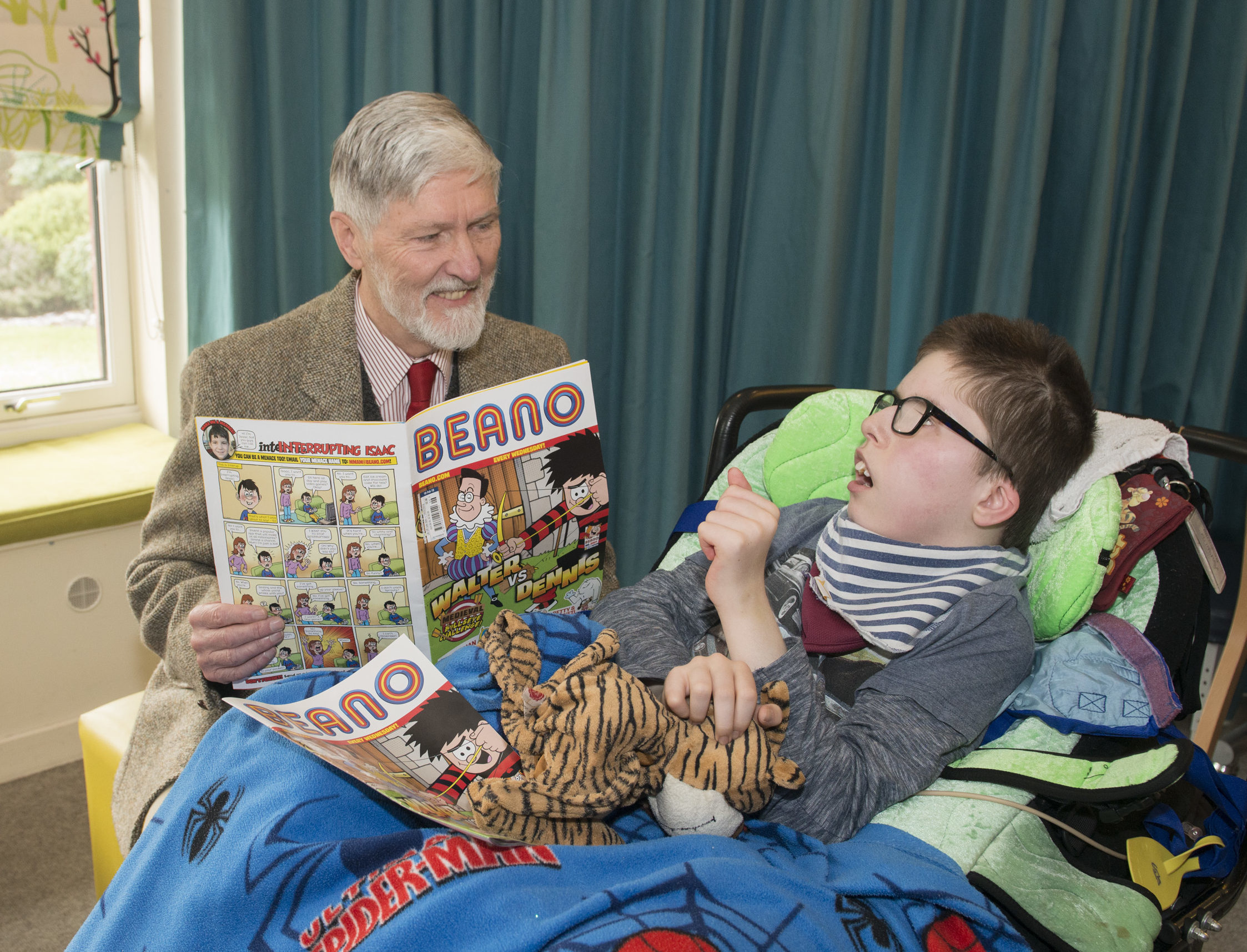 Pictured at Rachel House, poet Robin Bell reads a Beano comic to Brooklyn age 13