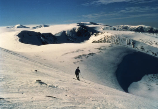 A lone skier surveys the surrounding peaks from Coire Cas in the Cairngorms.