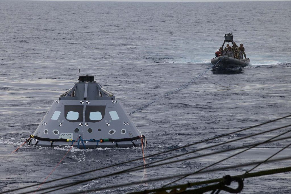 U.S. Navy divers and other personnel in a rigid hull Zodiac boat attach tether lines to a test version of the Orion crew module during Underway Recovery Test 5 in the Pacific Ocean off the coast of California. 