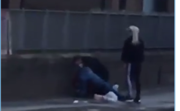 The footage shows the two men struggling on the ground while the woman looks on.