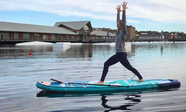 Instructor Michaella demonstrating a yoga pose on a paddle board at City Quay.