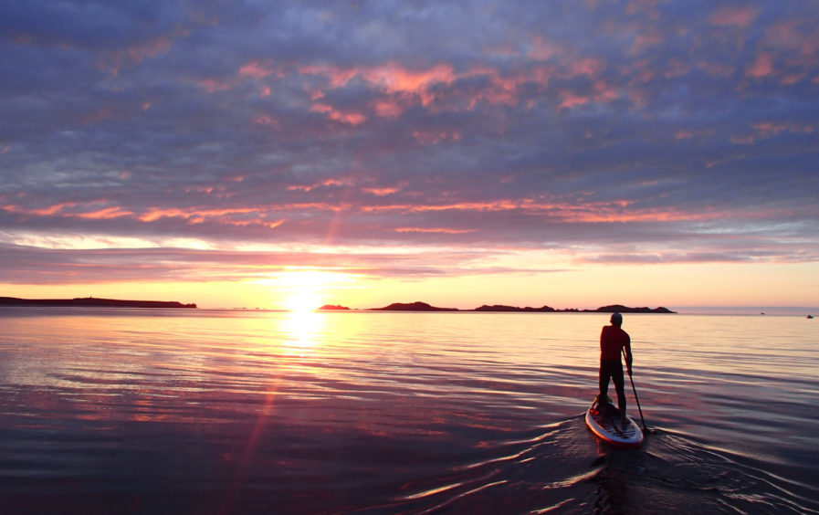 Loch tay at sunset with a solo stand up paddle boarder heading towards the light.