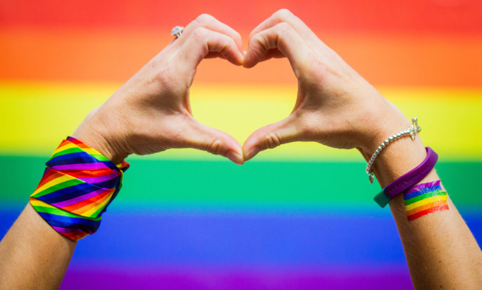 The hand heart with the pride flag in the background.