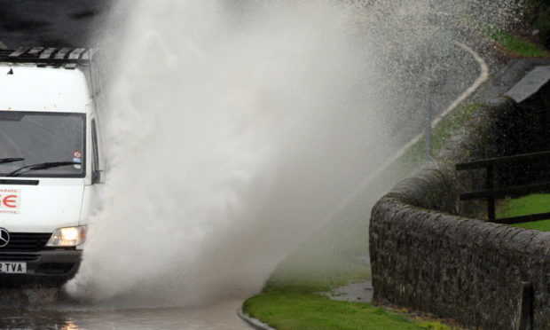 A van drives through surface water on a road.