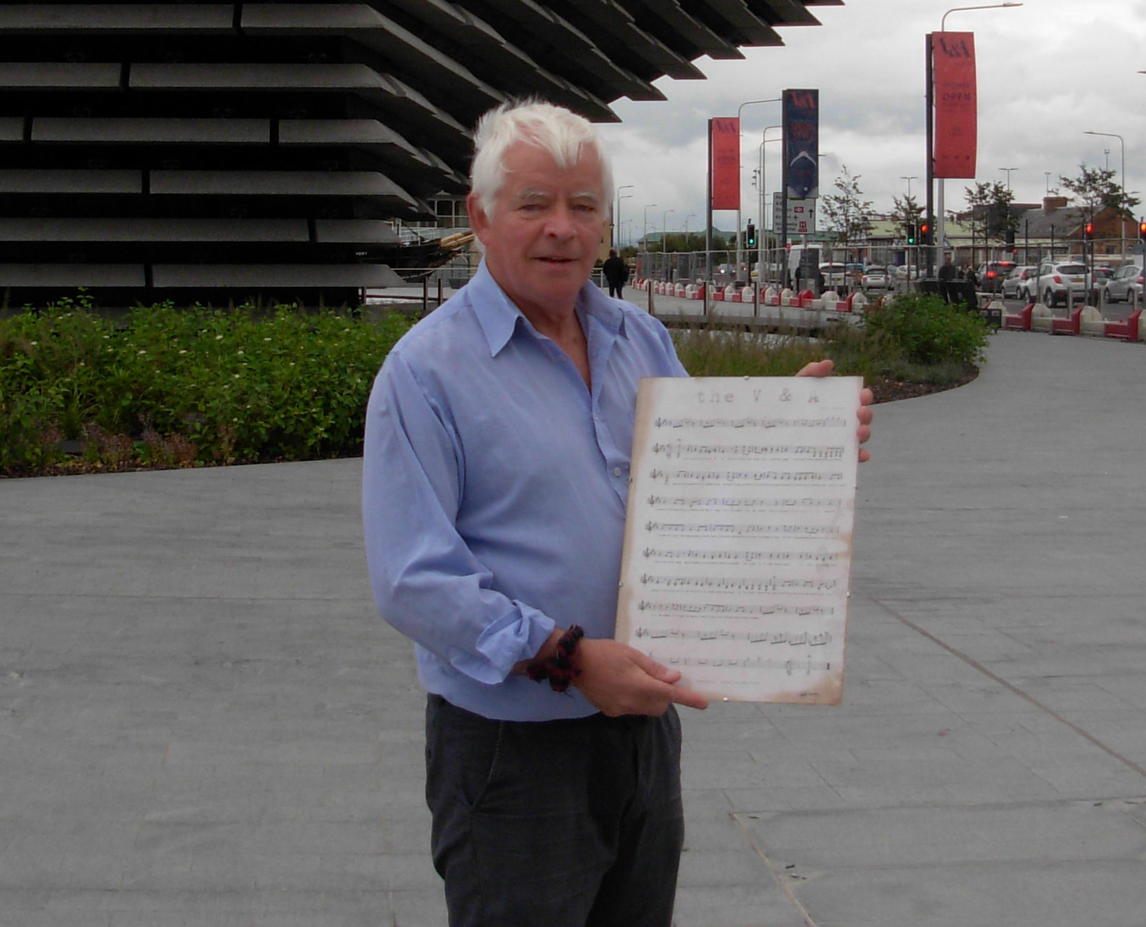 Eddie Cairney with a copy of his song in front of the V&A Dundee
