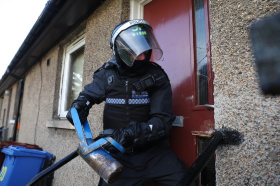 A police officer forcing entry to a property as part of the anti-drugs operation.