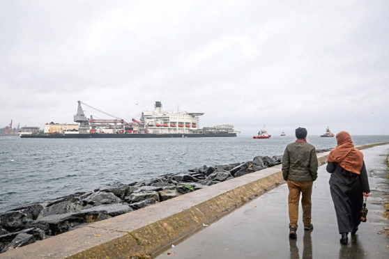 A man and a woman walk through the coastline as the Pioneering Spirit, the world's largest construction ship, passes through Bosphorus to lay natural gas pipe to the deepwater of TurkStream in Istanbul, Turkey on November 22, 2018.