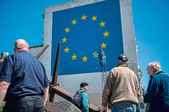 People view a mural by British graffiti artist Banksy, depicting a workman chipping away at one of the stars on a European Union (EU) themed flag on May 9, 2017 in Dover, England.