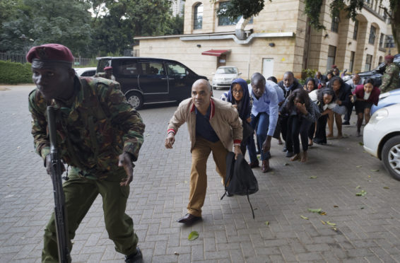 Civilians who had been hiding in buildings flee under the direction of a member of security forces at a hotel complex in Nairobi,. Terrorists attacked an upscale hotel complex in Kenya's capital Tuesday, sending people fleeing in panic as explosions and heavy gunfire reverberated through the neighborhood.
