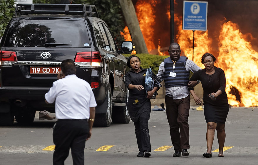 Security forces help civilians flee the scene as cars burn behind, at a hotel complex in Nairobi.