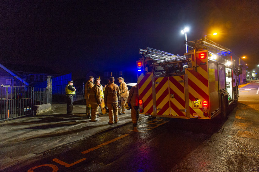 Firefighters standing beside engine at school gates in darkness