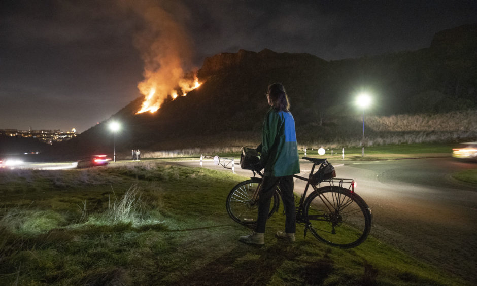 A cyclist takes in the scene of a gorse fire below Salisbury Crags in Holyrood Park, Edinburgh.