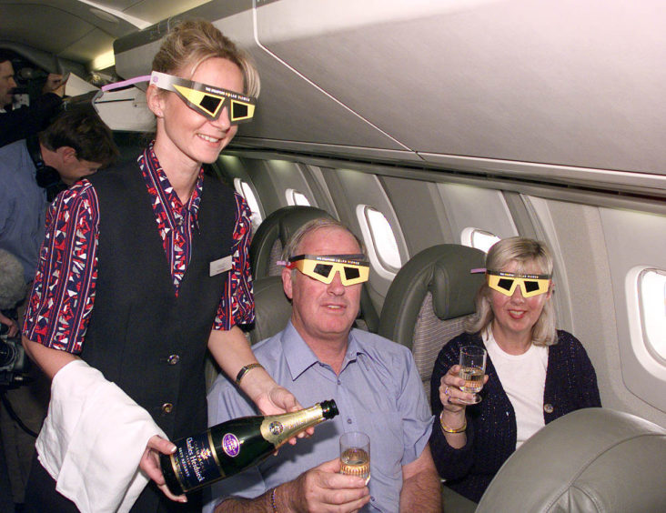 Gill and John Whiteside from Northamptonshire, wear protective glasses and enjoy a glass of champagne from stewardess Samantha Kingdon, as they speed along at 1,350 mph, aboard Concorde, for a special eclipse viewing trip in 1999.