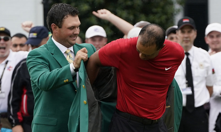 Patrick Reed helps Tiger Woods with his green jacket after Woods won the Masters golf tournament