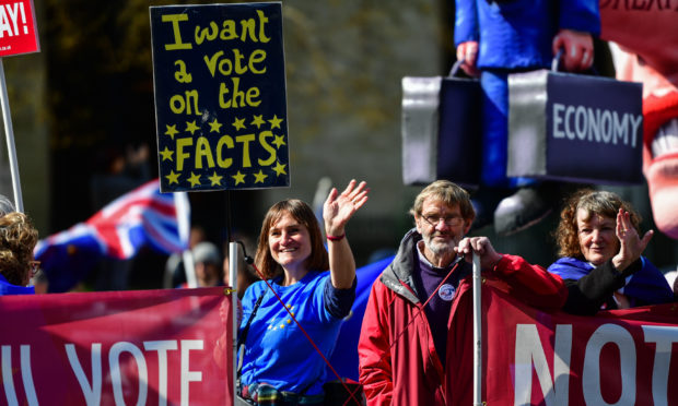 Members of the public wave to oncoming traffic holding a sign saying "I want a vote on the facts" outside the Houses of Parliament, Westminster.