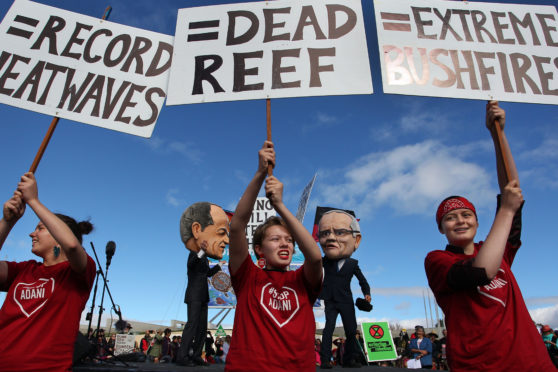 Young environment activists hold protest signs up in front of comedians dressed as Labour leader Bill Shorten and Prime Minister Scott Morrison in Canberra, Australia.