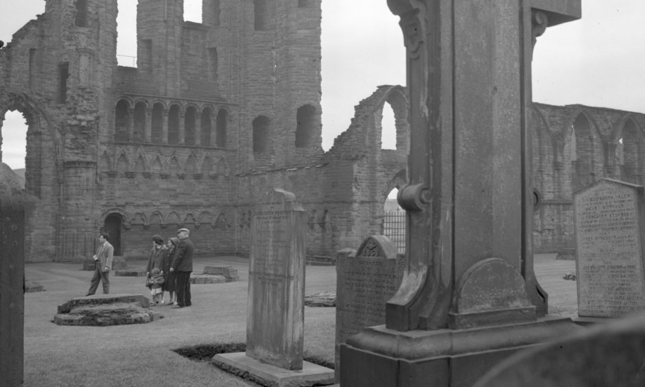 Visitors to Arbroath Abbey stand not far from the high altar, with the magnificent ruins of the South Transept and the round O of Arbroath in the background. At one period the Round O served as a beacon for mariners. 1963.