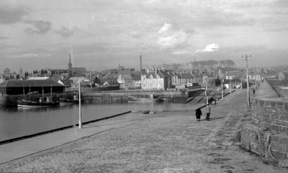 View of Arbroath Harbour from the harbour wall, overlooking the fishing boats to the town beyond. The ruins of Arbroath Abbey can be seen on the skyline on the left hand side. 1962.