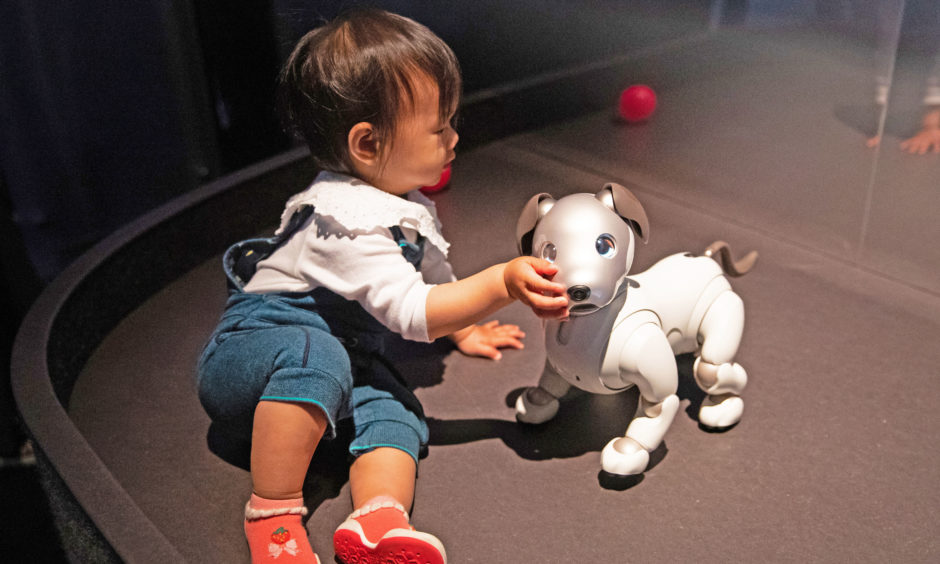 Charlotte Xie, aged one, interacts with Sony's robot puppy 'Aibo' at a press preview for AI: More Than Human exhibition. The major new exhibition explores the relationship between humans and artificial intelligence.
