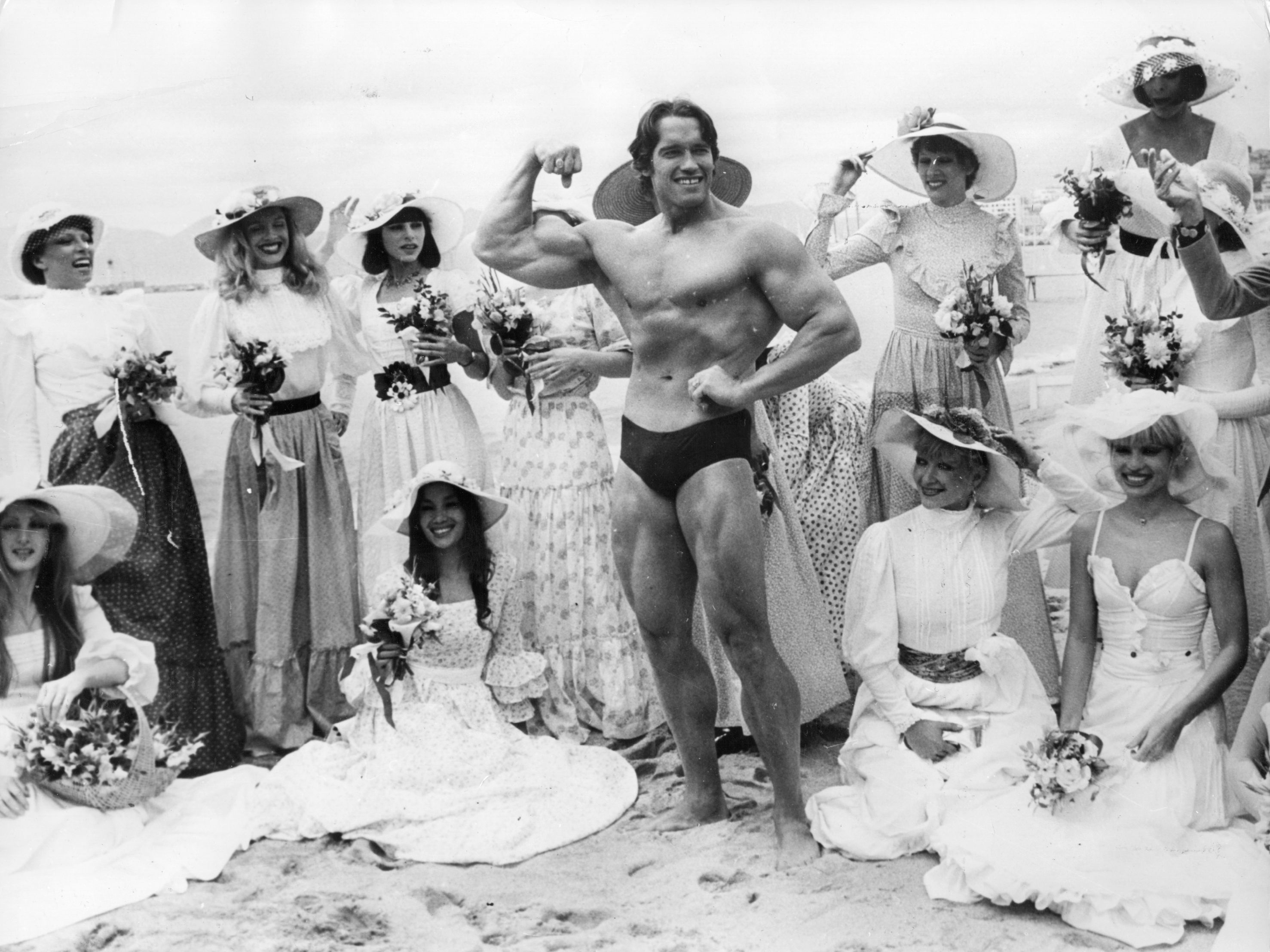 Arnold Schwarzenegger, the film actor who first became famous as Mr Universe for his magnificent physique, on Cannes beach during the Film Festival with the girls from the Folies Bergere.