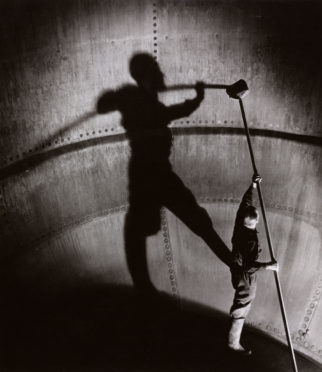 A brewery worker casts a giant shadow as he cleans inside a copper coffer. Taylor-Walker Brewery, Manchester.