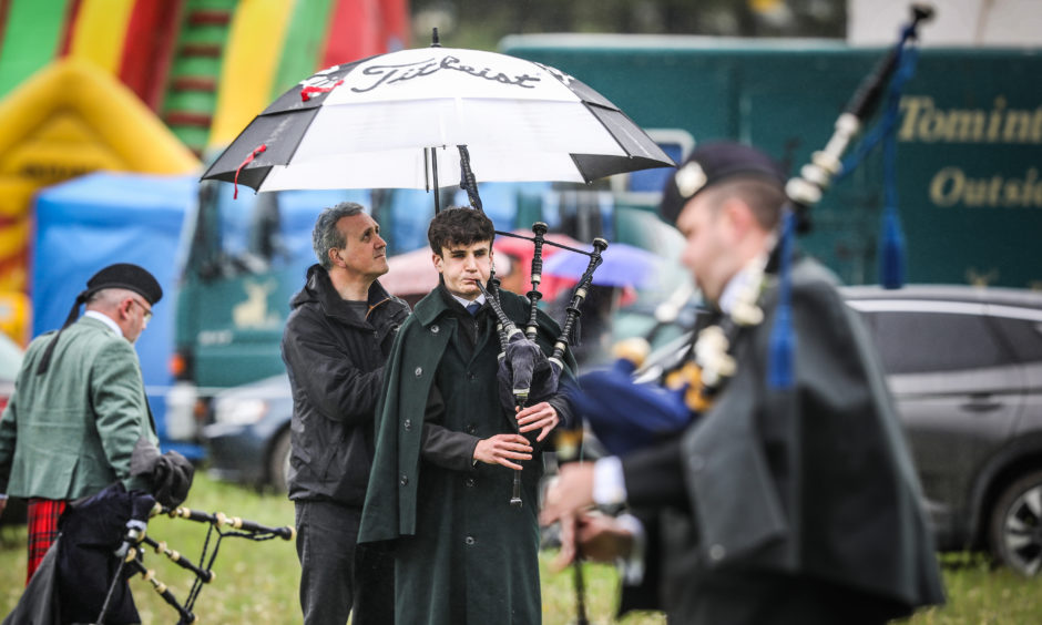 Andrew Ferguson, 17, tunes up his bagpipes while his dad Stuart holds an umbrella for him.