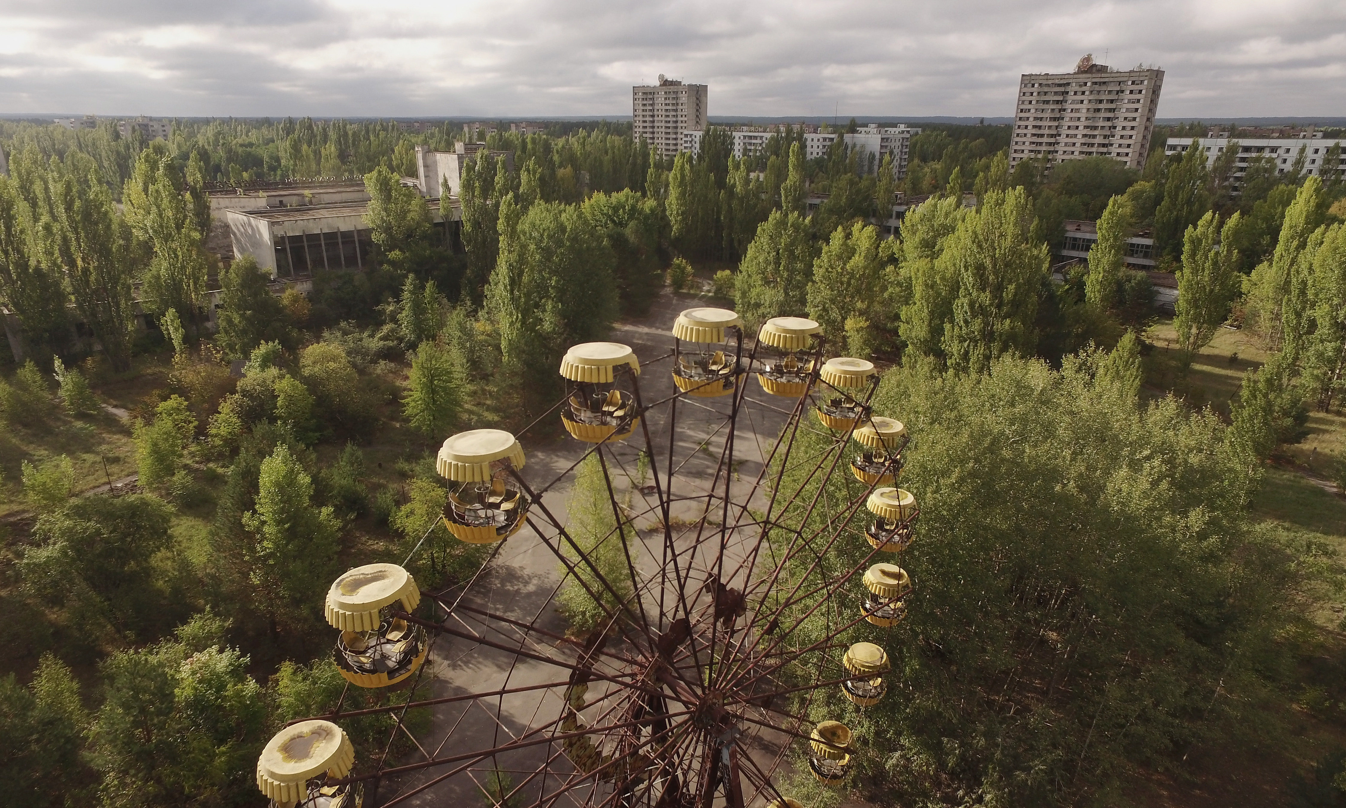 An abandoned ferris wheel stands on a public space overgrown with trees in Chernobyl.