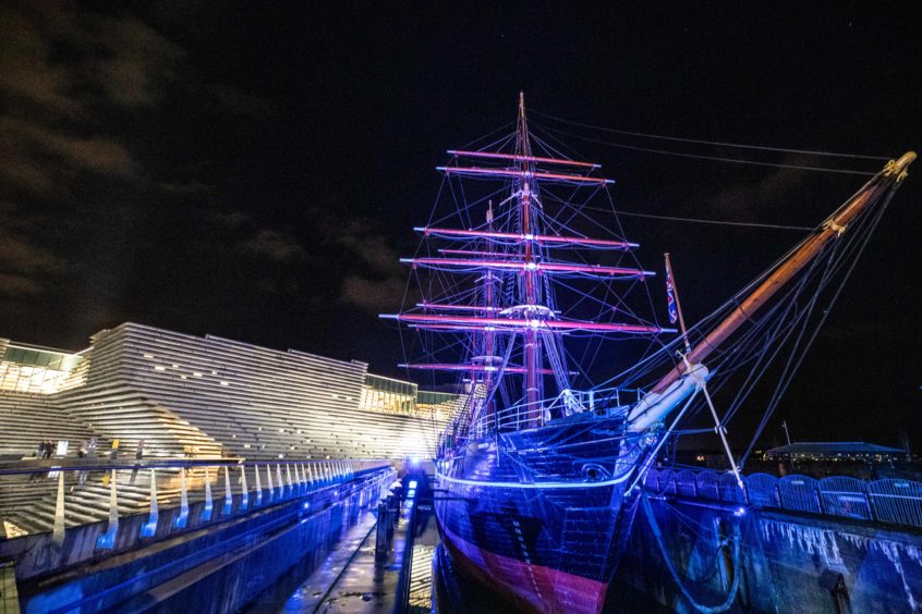 RRS Discovery lit up at night next to the V&A Dundee museum.