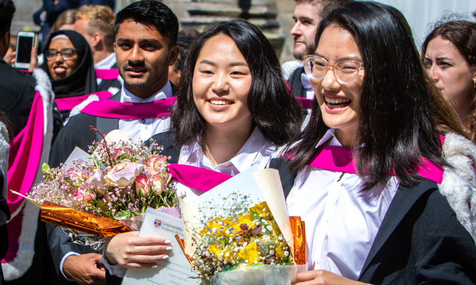 Graduates hold celebratory flowers.