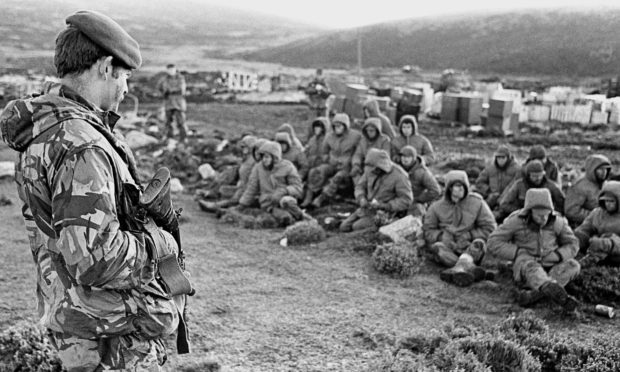 Argentinian soldiers captured at Goose Green are guarded by a British Royal Marine as they await transit out of the area.