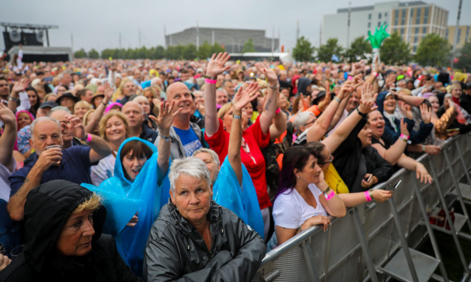 Crowds of people wait for Sir Tom Jones in the rain.