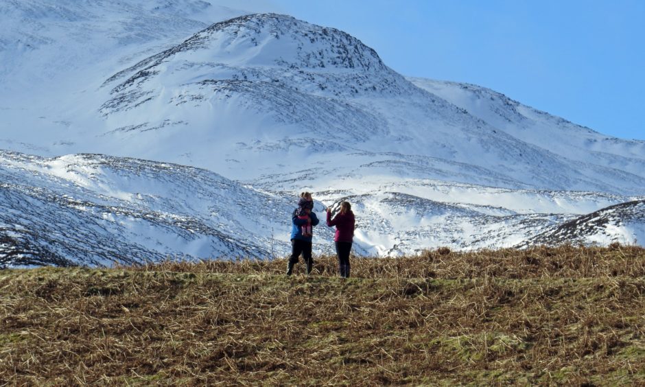 Two people on Schiehallion with snow covered mountaintop in front