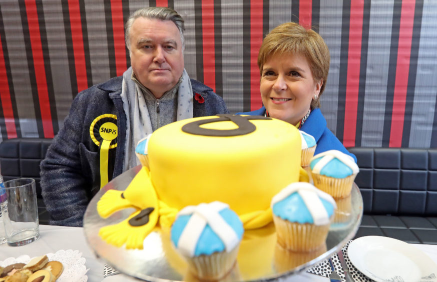 Nicola Sturgeon and John Nicolson in front of a display pf cakes decorates in the SNP symbol and saltire flag