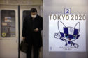 A poster promoting the Tokyo 2020 Olympics is posted next to a train door as a commuter wearing a mask looks at his phone.