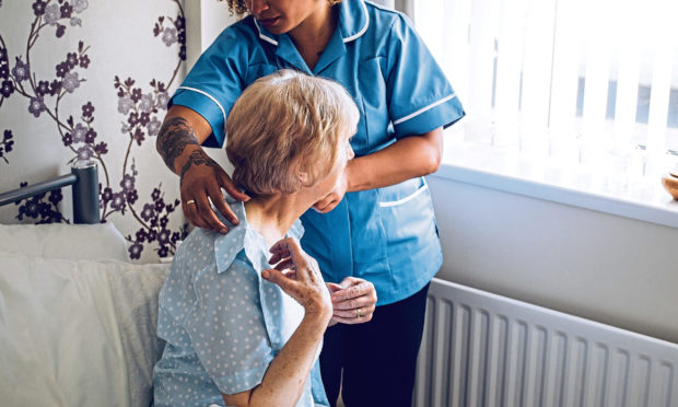 Home Caregiver helping a senior woman get dressed in her bedroom