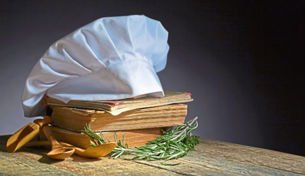 Old culinary books , chef hat and wooden spoons . Kitchen accessories on the old wooden table .; Shutterstock ID 719175079; Purchase Order: -