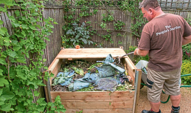 A wooden compost bin made from a kit supplied by Harrod Horticultural being filled with material suitable for home composting.