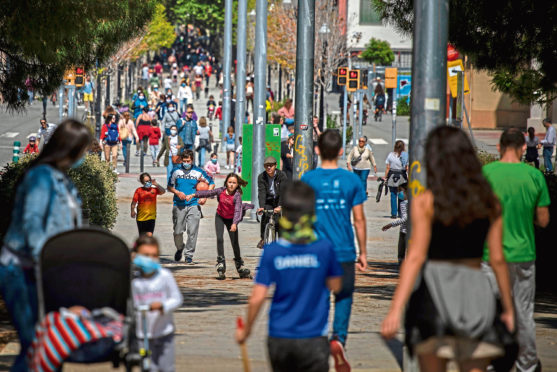 Families walk along a boulevard in Barcelona, Spain, Sunday, April 26, 2020, as the lockdown to combat the spread of coronavirus continues. Spain's government has let children out after 44 days behind doors on Sunday, starting at 9:00 local time. Children under 14 years old are now allowed to take walks with a parent for up to one hour and within one kilometer from home, ending six weeks of compete seclusion. (AP Photo/Emilio Morenatti)