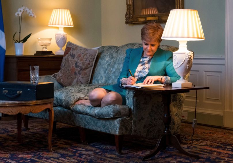 Nicola Sturgeon, feet up on a sofa, writing in a journal, in her official residence Bute House.