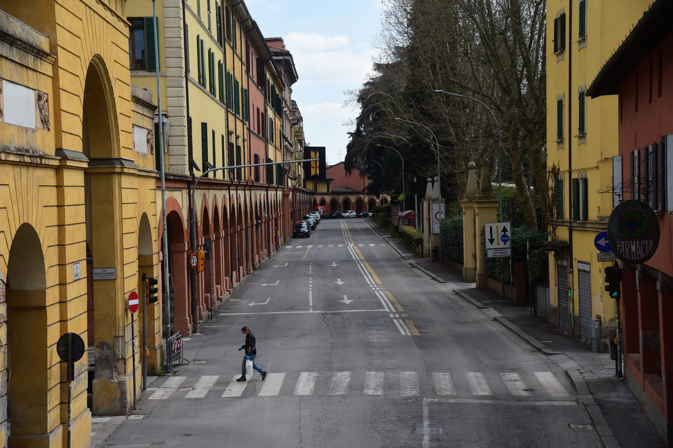 A man in a facemask walks across a street in Bologna.